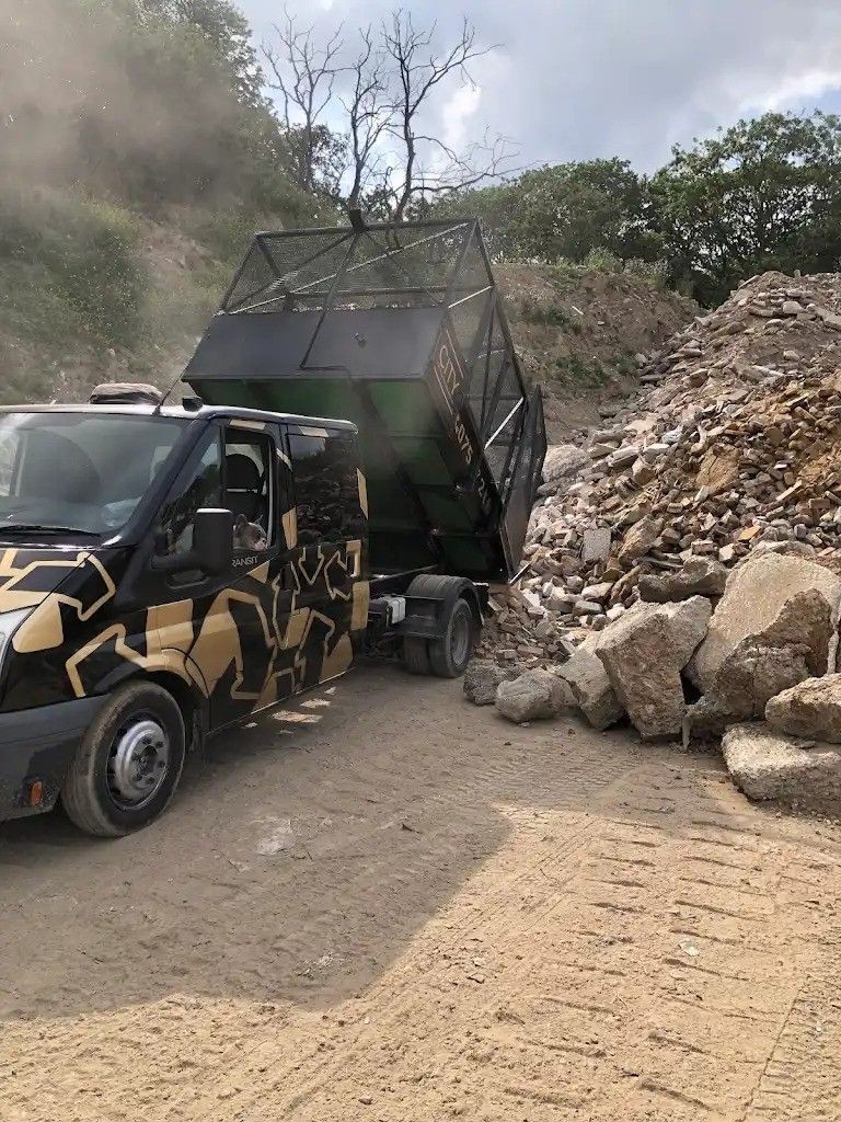 Van with geometric design unloading rubble at a construction site with trees in the background.